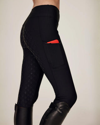 Side view of black riding breeches showing the practical phone pocket with a red mobile phone inside for size reference.