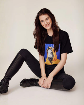 Relaxed sitting model wearing the black riding breeches paired with a black horse print t-shirt.