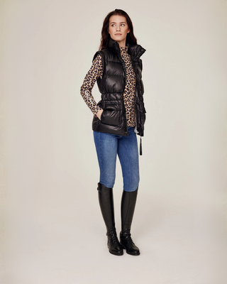 Helkroppsbild från sidan av den öppna svarta ridvästen stylad med en komplett leopardmönstrad ridoutfit.
