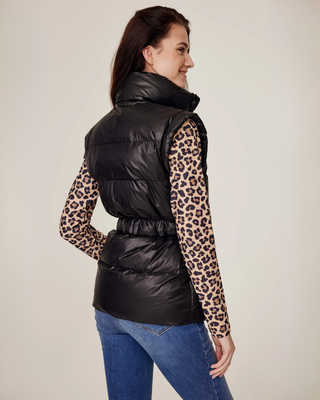 Profilbild från sidan av modellen som bär den halvblanka svarta puffervästen och en leopardmönstrad ridtopp.
