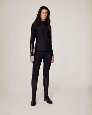 Angled full body shot of a model styling the black riding top with matching black riding tights for a sleek look.