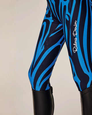 Detailed shot of the left leg featuring the white "Riders Denim" logo on the blue zebra print.