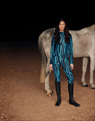 Equestrian lifestyle shot of a model in the blue zebra set with a grey horse in the background.