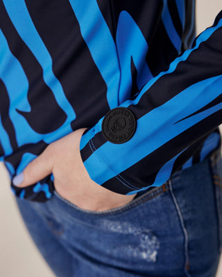 Närbild av ärmen med Riders Denim-loggan på blått zebratyg, med modellens hand i fickan på hennes denim-ridbyxor.