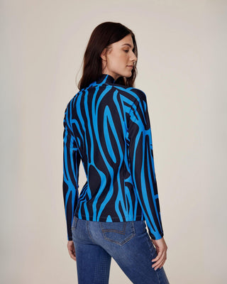 Angled back view of a model wearing the blue zebra riding top with a high collar, paired with original denim breeches.