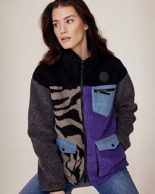 Sitting model posing with one arm behind her back, showcasing the zipped-up lilac and zebra print riding jacket.