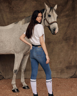 Model seen from behind with a grey horse, wearing Riders Denim original jeans breeches, white riding socks, and a white horse print t-shirt.