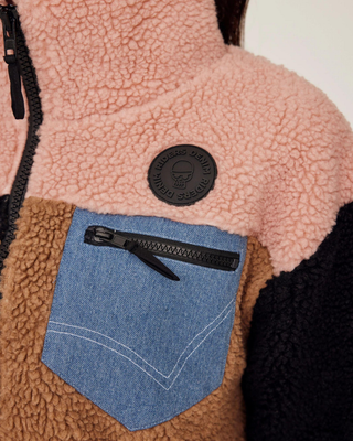 Detaljerad bild av bröstfickan med dragkedja och den signaturpräglade Riders Denim-logotypen på den rosa panelen.