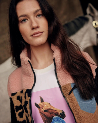 orträtt av en modell i den rosa och leo teddyjackan och vit t-shirt med hästtryck med en grå häst i bakgrunden.