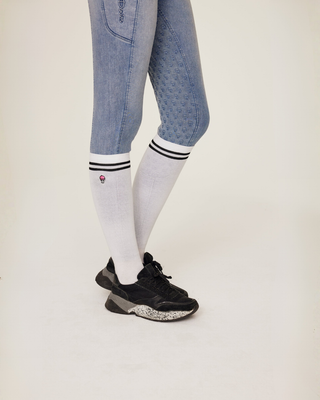 Close-up of a rider’s leg in light blue denim breeches paired with white riding socks with black details.