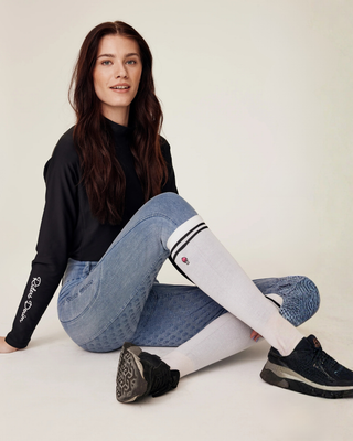 Model posing in a relaxed sitting position, highlighting the complete equestrian outfit with white riding socks.